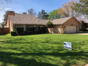 A large single-family home features a lush lawn, stone siding, and a brown asphalt shingle roof.