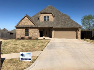 A luxury home with brown stone siding and a gray dimensional shingle roof.