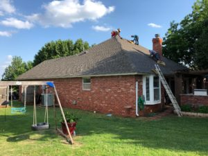 Roofers work to inspect the shingle roof of a one-story residential home.