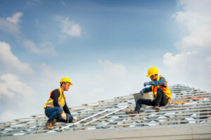 Construction worker wearing safety harness belt during working on roof structure of building on construction site,Roofer using air or pneumatic nail gun and installing concrete roof tile on top new roof.