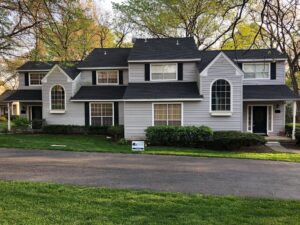 Large, light gray suburban home with dark shingle roofing